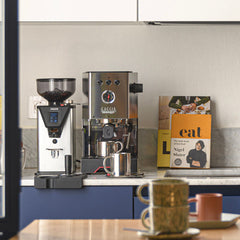 Stainless steel Gaggia Classic UP espresso machine and Gaggia grinder on a kitchen counter with milk jugs and cookbooks.
