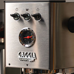 Close-up of the stainless steel Gaggia Classic UP front panel with toggle switches, pressure gauge and logo.
