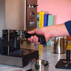 Hand holding the portafilter in the group head of a stainless steel Gaggia Classic UP espresso machine.