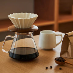 Coffee brewing setup with a glass carafe, coffee filter, and cup on a wooden table.