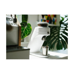 White Mahlkönig X64 SD espresso grinder on an espresso bar with plants