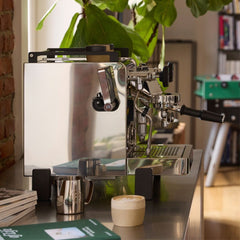 Side view of the Rocket R58 TUNE on a kitchen counter beside a milk jug and a cup of coffee.