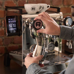 Hand operating the Rocket R58 TUNE steam control knob while holding a milk jug beneath the steam wand.