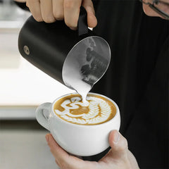 Barista pouring latte art into white cup with black Timemore Rosetta Pro Milk Pitcher
