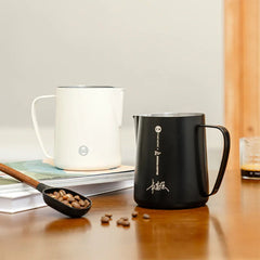 Timemore Rosetta Milk Pitcher black & white side-by-side on desk with coffee beans