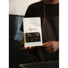 Person wearing an apron holding a bag of Rosetta Roastery Caballero La Arcadio coffee.