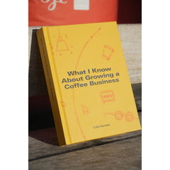 What I Know About Growing a Coffee Business by Colin Harmon propped on a wooden bench, showing its yellow cover and spine.