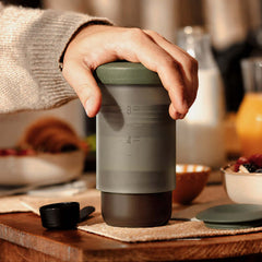 Hand pressing a Sage Green Wacaco Prestina to brew coffee into its cup on a breakfast table.