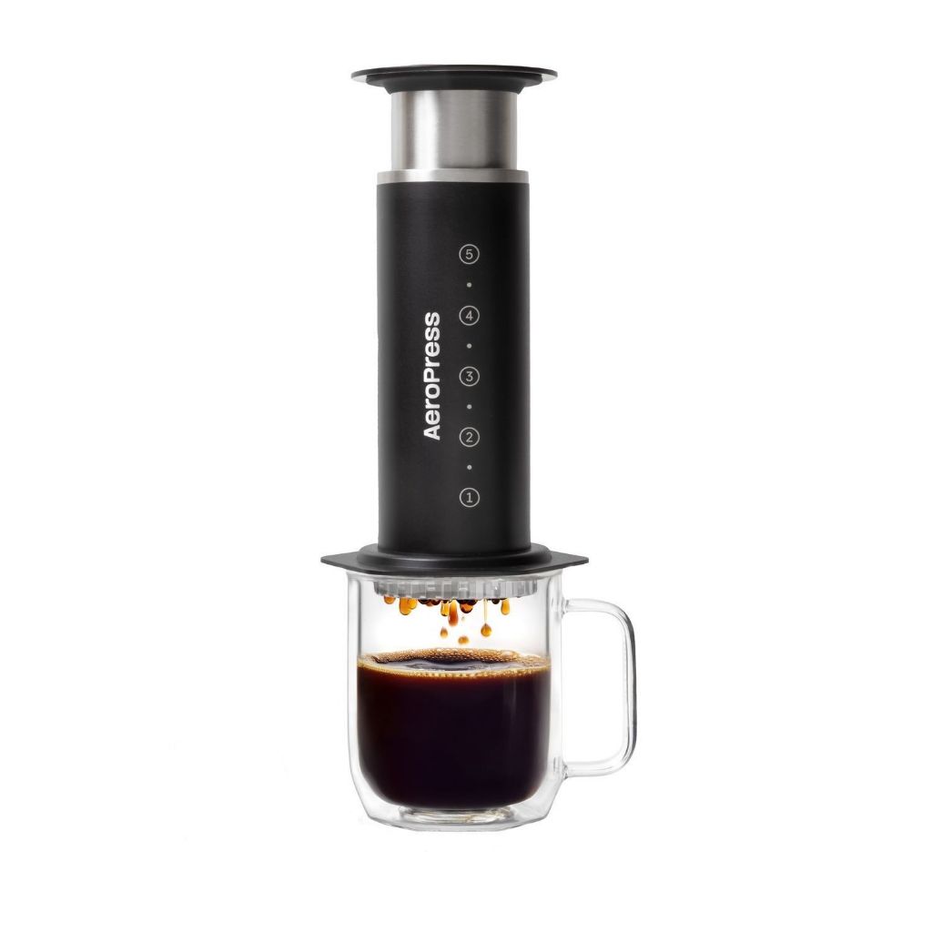 Black AeroPress Stainless Steel Coffee Press brewing coffee into a clear glass mug.