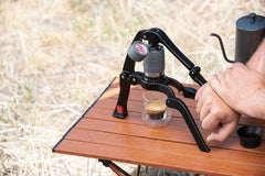 Person using a Flair Go Espresso Maker on a wooden table outdoors.