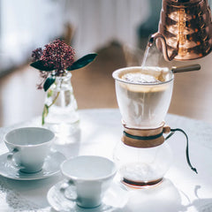 Table scene with hot water pouring into Hario Drip Pot Woodneck coffee brewer