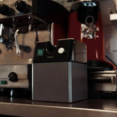 Kaffee Klar T1 Automatic Portafilter Cleaner next to espresso machine in a café scene