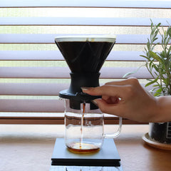 Hario Mugen Switch dripper in use on a bar with a hand opening the valve