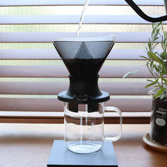 Hario Mugen Switch dripper in use on a bar with plants behind it