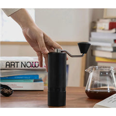 Nuttii X Timemore Goosey Hand Grinder 38mm Black on desk with books, hand & coffee carafe