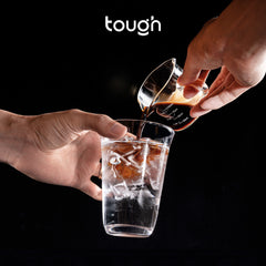 Hands pouring coffee from Tough Double Spout Espresso shot glass into glass with water & ice