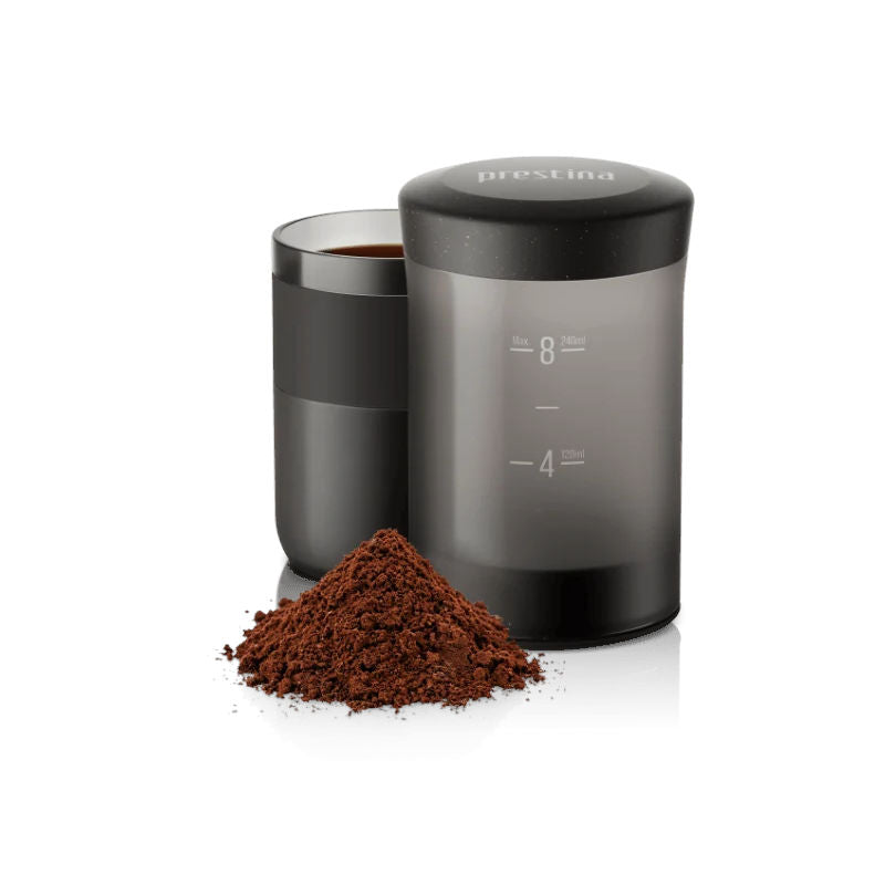 Wacaco Prestina portable coffee maker beside its coffee-filled cup and a pile of ground coffee.