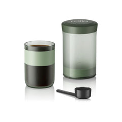 Wacaco Prestina brewing chamber beside a cup of black coffee and the included scoop.